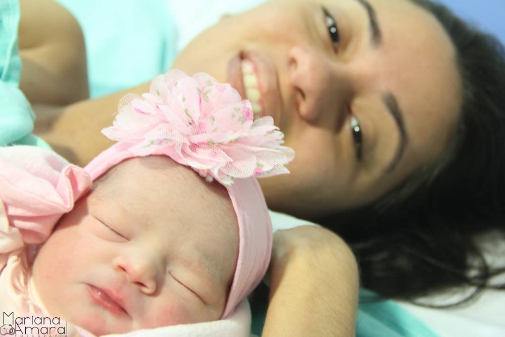 Foto da Mariana ao fundo após o parto e da filha recém nascida Clara usando laço rosa