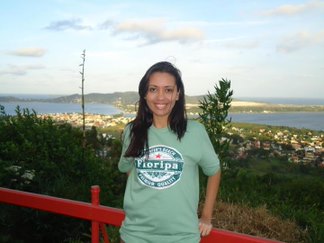 Foto da Mariana com camisa verde e um fundo com natureza e praia